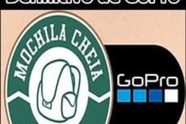 Homem sorridente filmando com câmera GoPro Hero 11 em uma trilha na montanha com mochila nas costas, paisagem exuberante ao fundo, luz dourada do pôr do sol.